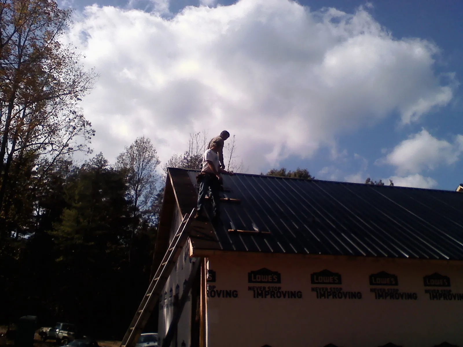 Roofer fastening dark metal panels high against a cloudy sky, from a Roof Inspection job in Occoquan