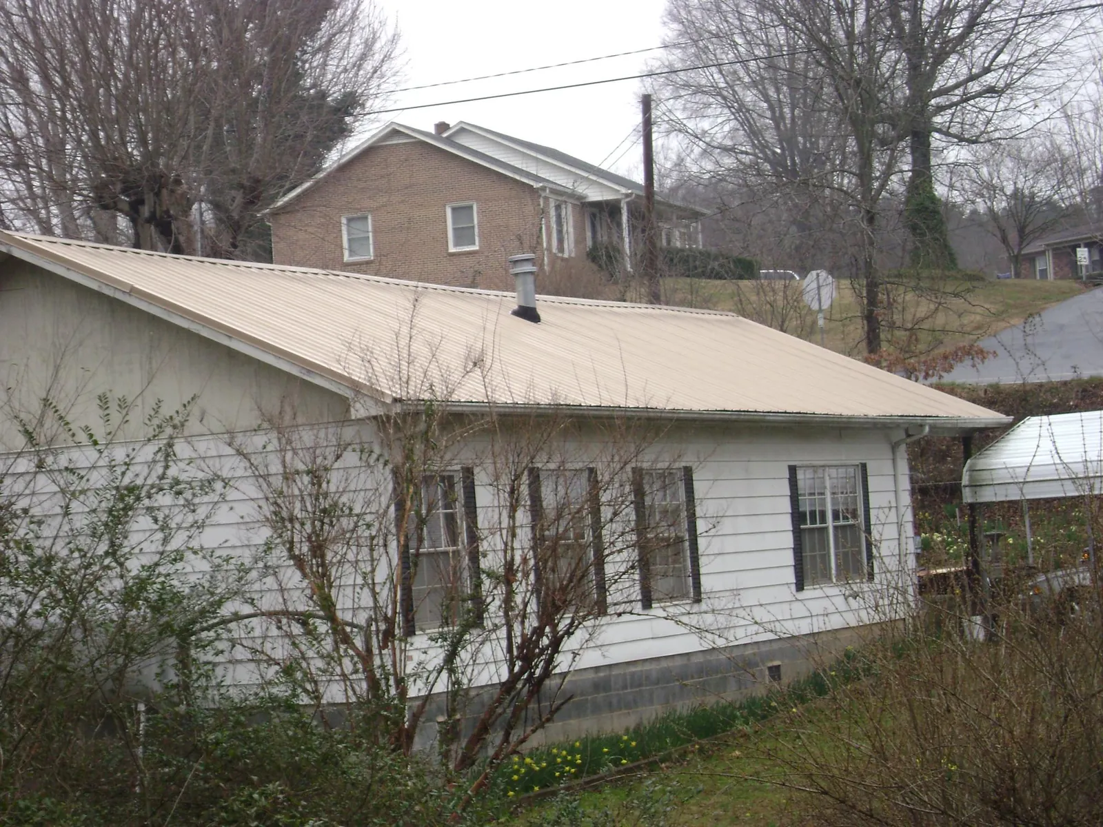 Tan metal roof on a white sided house set into a hillside — Commercial Roofing by Roofing Brothers in Occoquan